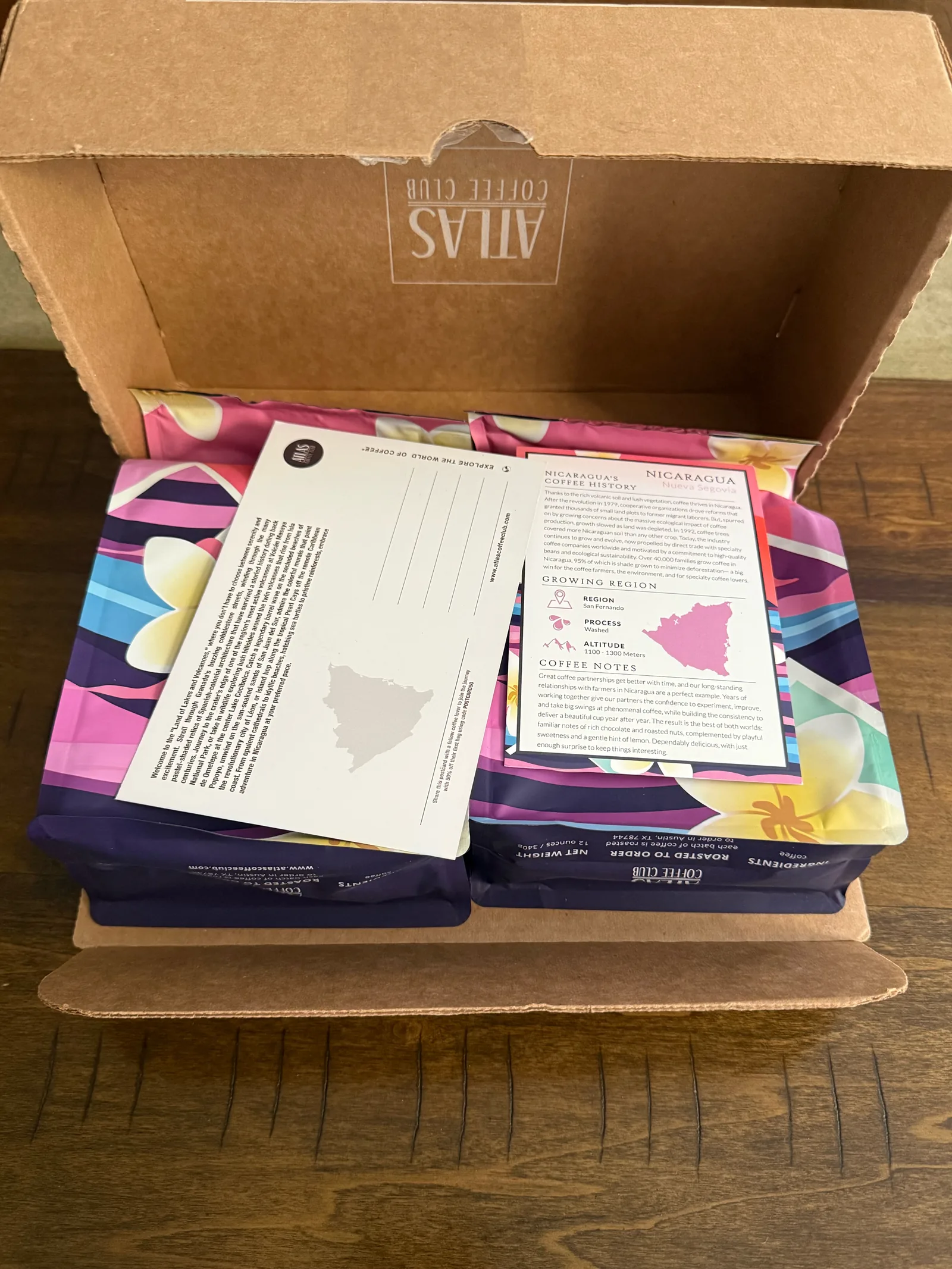 Open Atlas box with two pink and purple coffee bags, a Nicaragua postcard and the origin card on top