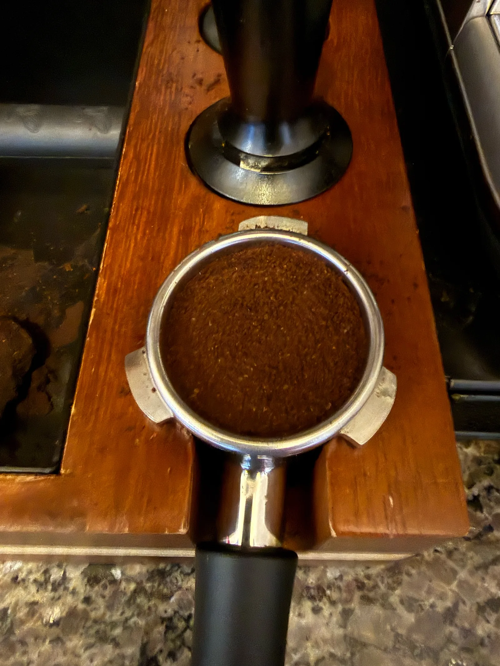 Portafilter of ground Atlas Nicaragua coffee on a wooden tamping station