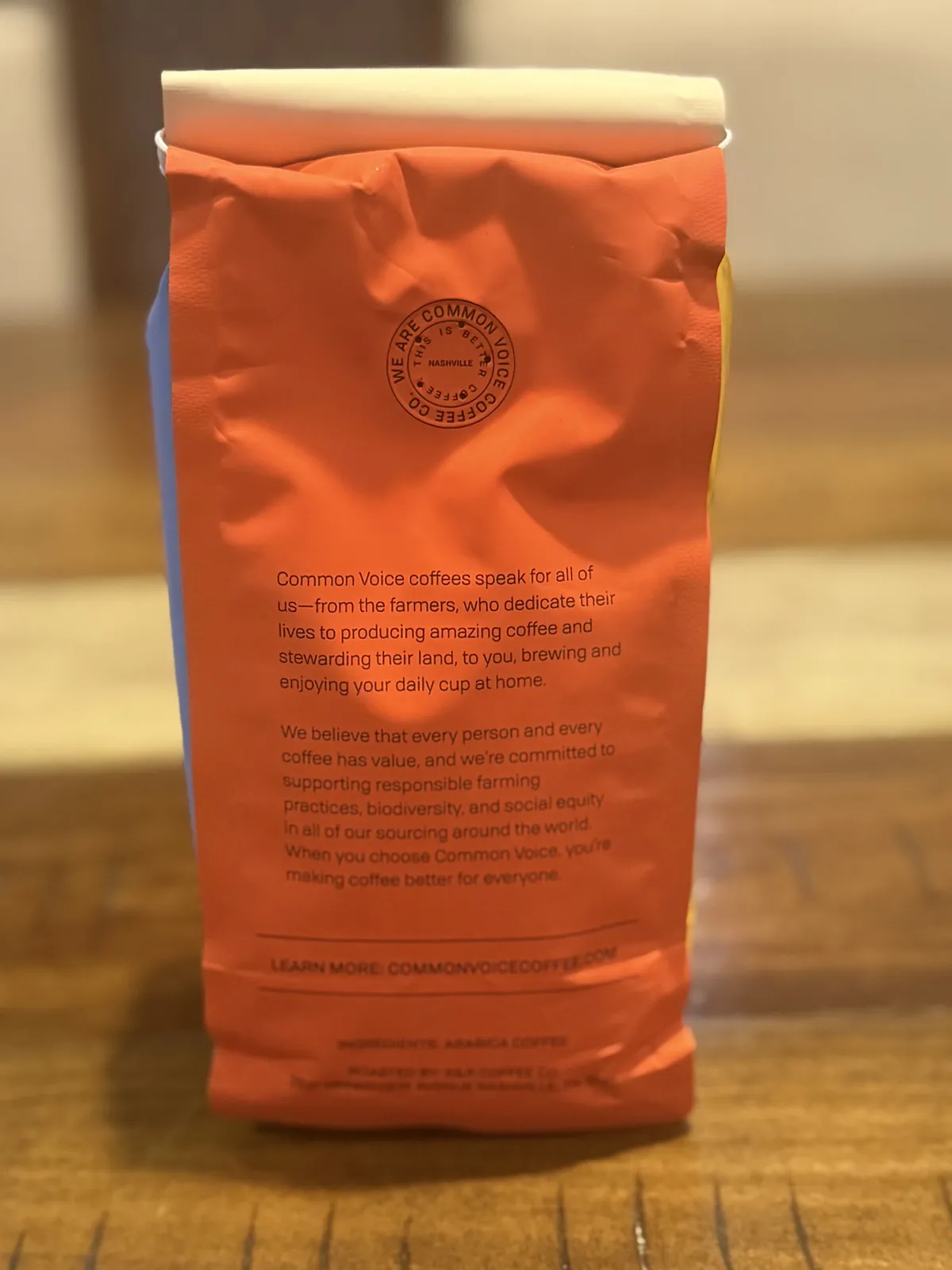 Orange back of the Common Voice bag with the brand's mission text and a "We are Common Voice Coffee Co." stamp