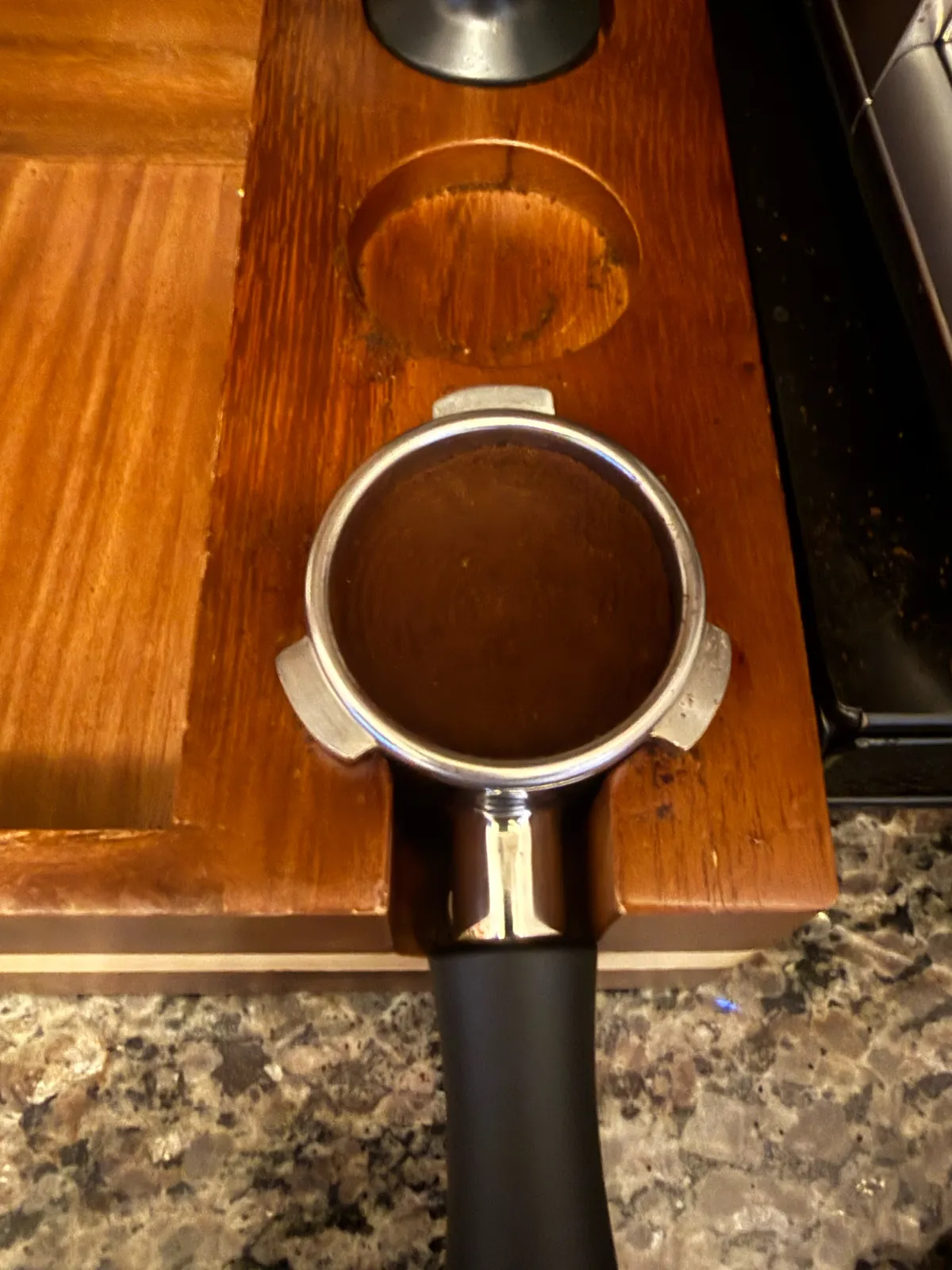 Tamped puck of Volcanica coffee in a portafilter on a wooden tamping station